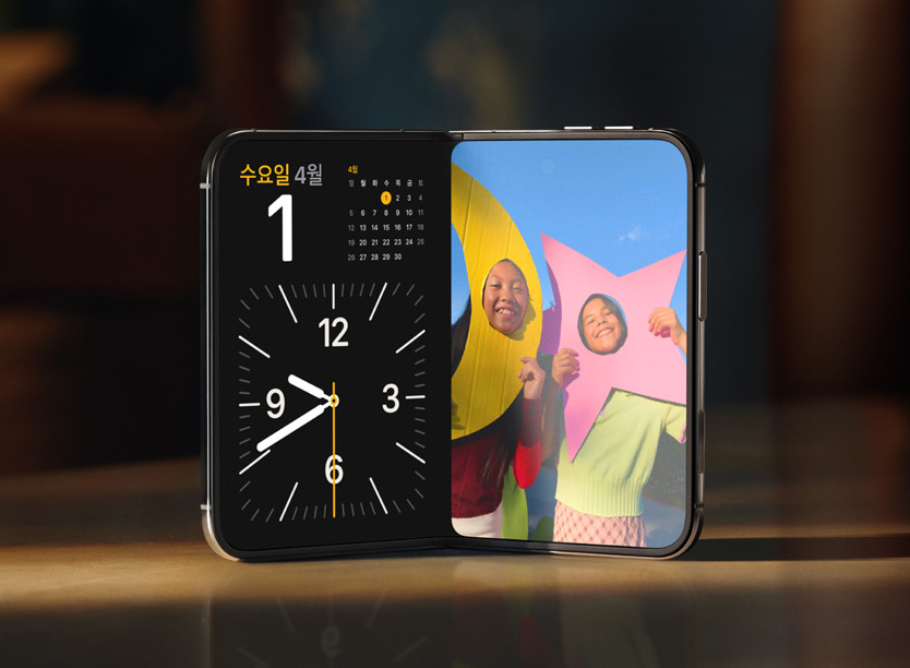 책상 위에 세워 둔 iPhone Duo. 왼쪽 화면에는 시계와 캘린더, 오른쪽 화면에는 사진이 나란히 표시된다.